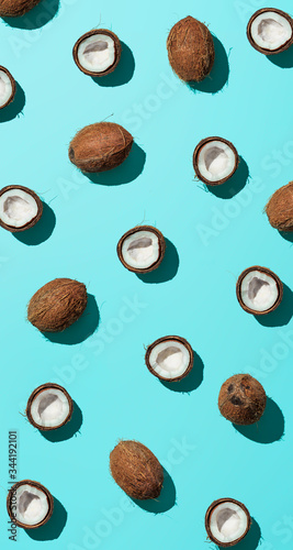 Creative layout of coconuts half on blue background. Tropical pattern, top view or flat lay. Hard light pop art minimal summer background. Vertical banner