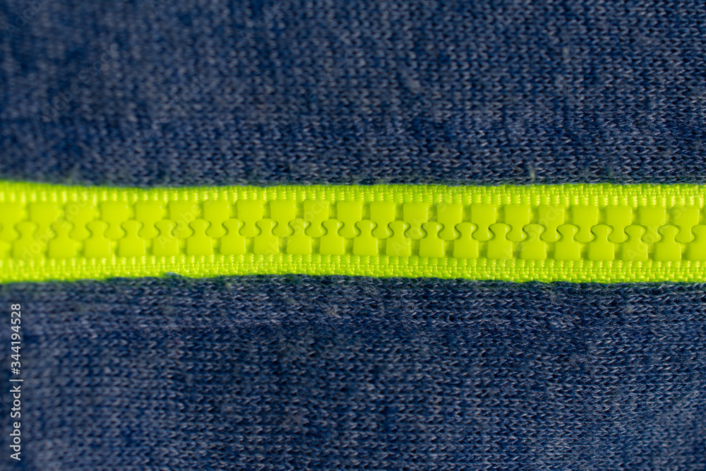 Bright green plastic zipper on a blue fabric texture, going from left to right Bright green plastic zipper on a blue fabric texture, going from left to right