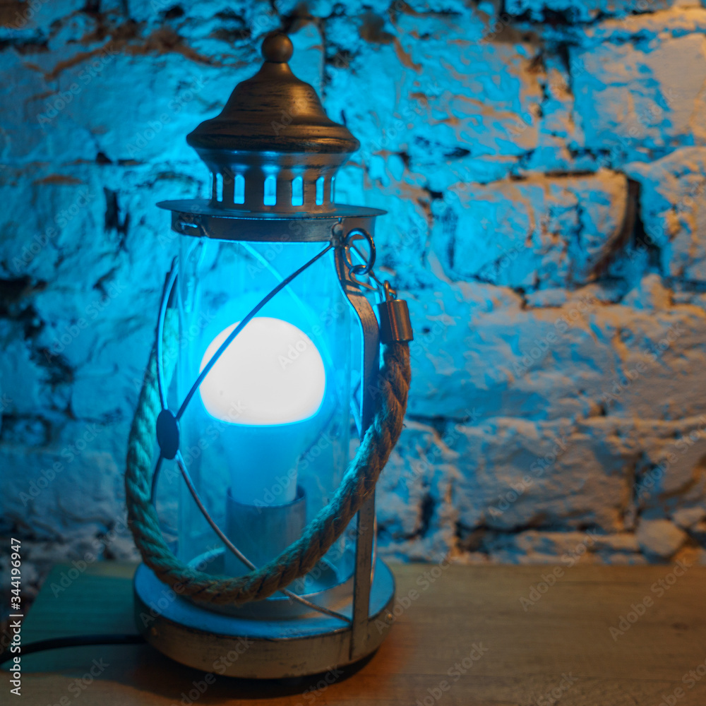 Close-up vintage table lamp shines blue light on brick wall background.