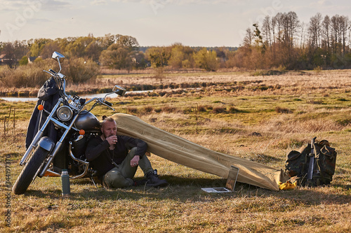 A traveler on a motorcycle talking on the phone working on a laptop admires the sunset