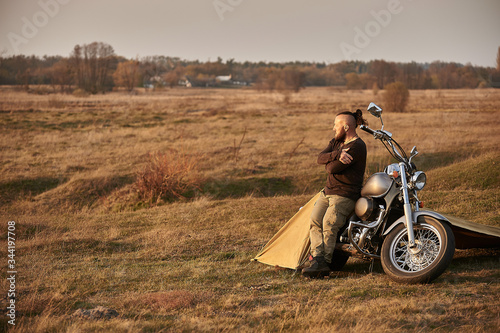 A traveler on a motorcycle talking on the phone working on a laptop admires the sunset