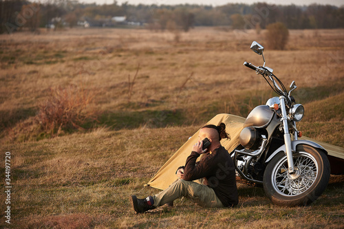 A traveler on a motorcycle talking on the phone working on a laptop admires the sunset
