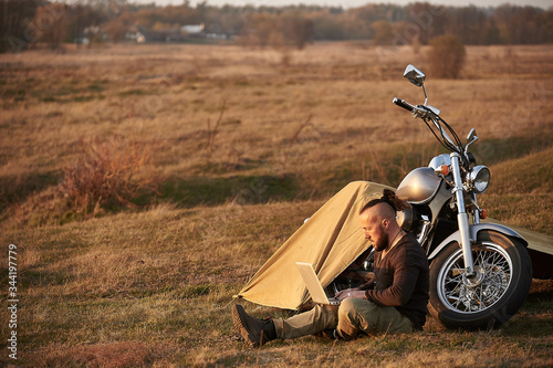 A traveler on a motorcycle talking on the phone working on a laptop admires the sunset