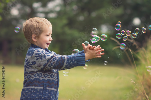 little boy is catching soap bubbles on the countyside and smiling