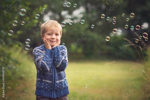 little boy is catching soap bubbles on the countyside and smiling