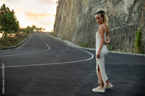 A beautiful girl with a bandana on her blond hair, sitting on an unusual black road in the mountains, this is a landmark of the island of Bali. The model is stylishly dressed in sneakers. Woman enjoys © evgennish
