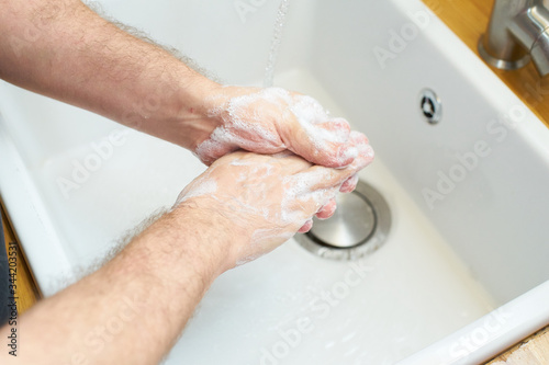 Man washing hands with soap by the kitchen sink. Adult person preventing virus spread. Personal hygiene