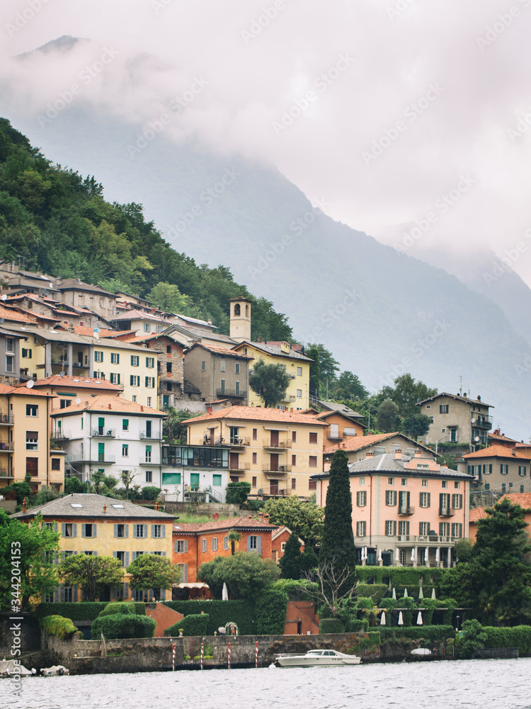 Italy. Lake Como. Green high mountains in the clouds with small houses and villages in red, yellow and white colors. down below is Lake Como. Overcast
