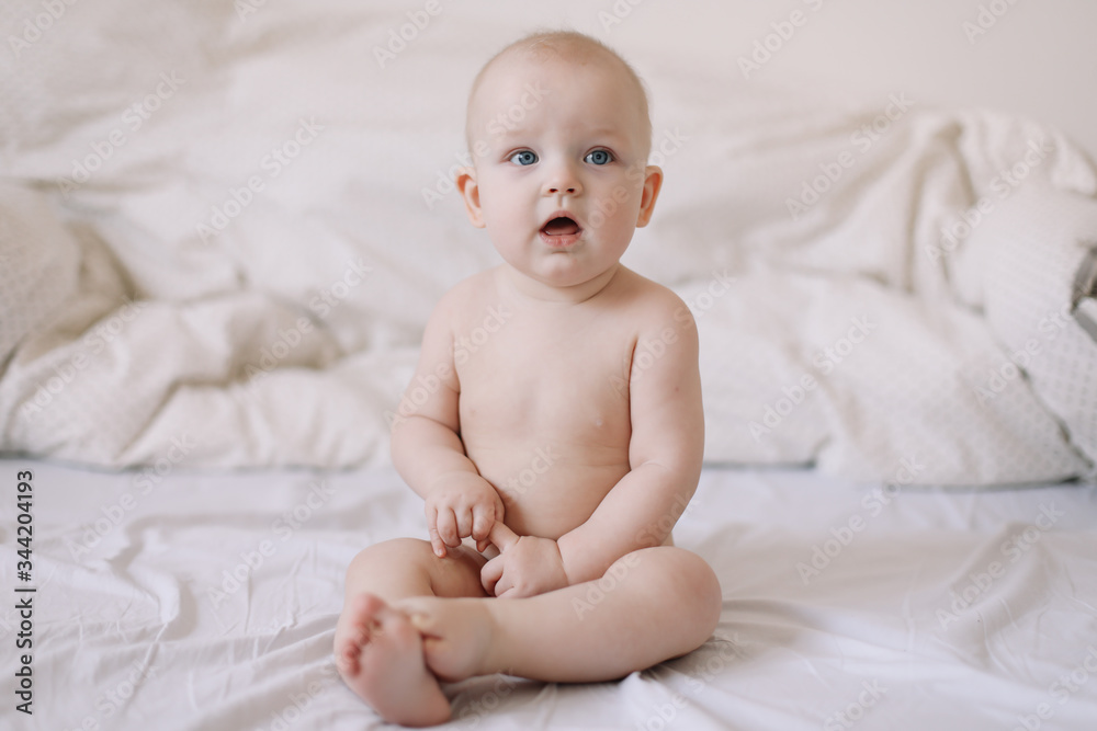Cute smiling baby sits on the bed. happy naked baby. children under one year old. baby girl playing, smiling, posing on the bed Cute smiling baby sits on the bed. happy naked baby. children under one year old. baby girl playing, smiling, posing on the bed
