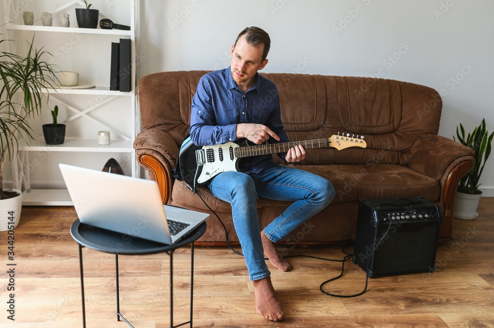 Online studying, webinars. A young man is shows how to play electric guitar to laptop webcam. Online tutor