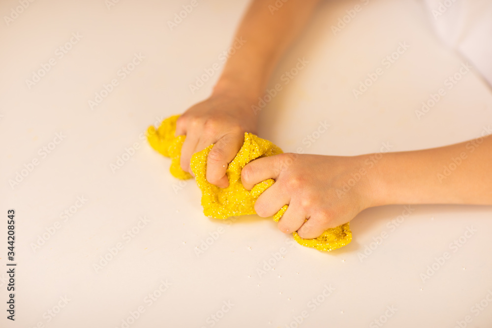 Obraz premium Girl's hands stretching yellow slime on white table