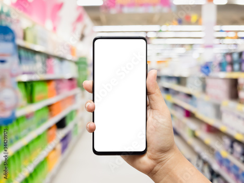 Mockup mobile phone with blank white screen. Hand holding smartphone with blurred supermarket background for your online application shopping.