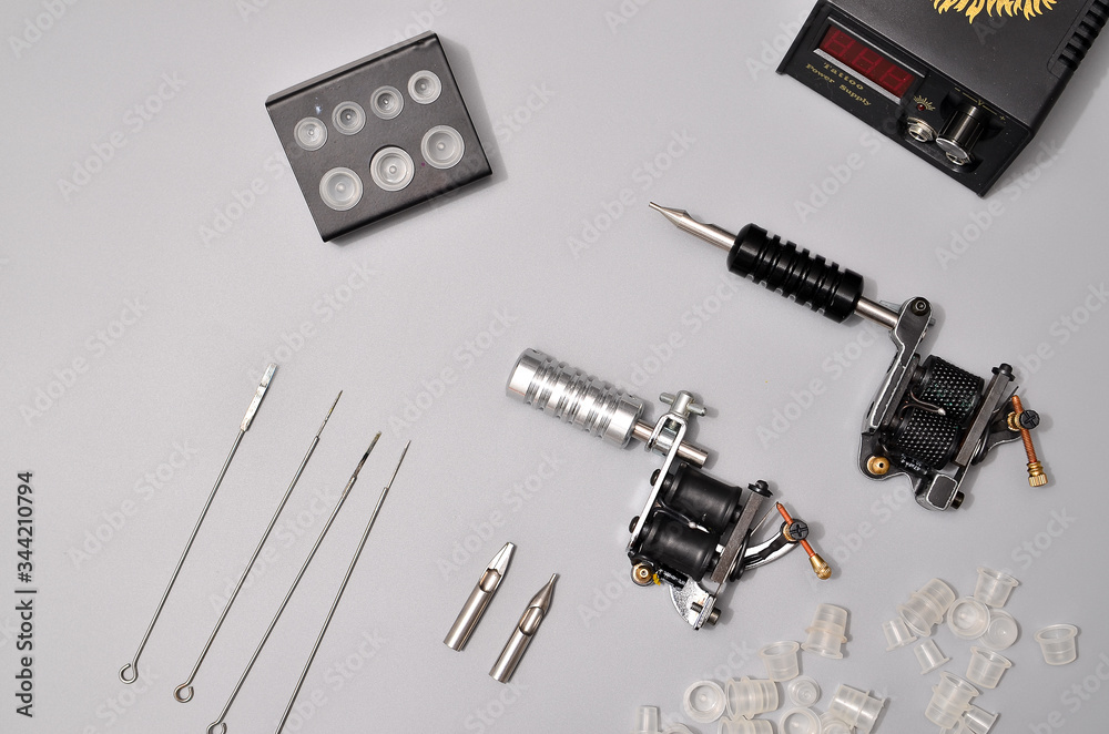 Tattoo machines, needles and all these tattoo stuff isolated on grey background. Tattoo guns. Pattern with tattoo machine, wallpaper for your business design Tattoo machines, needles and all these tattoo stuff isolated on grey background. Tattoo guns. Pattern with tattoo machine, wallpaper for your business design