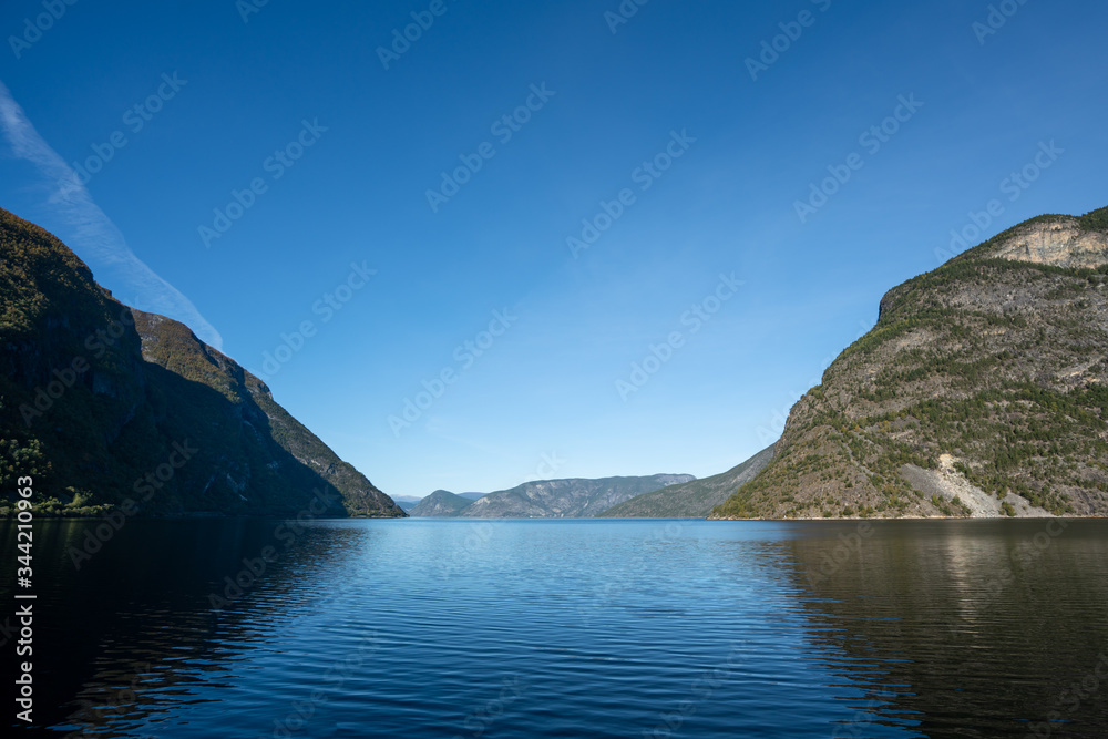 Water and mountains with blue skies in the fjords of the Aurlandsfjord in Aurland on a sunny day in southern Norway during autumn