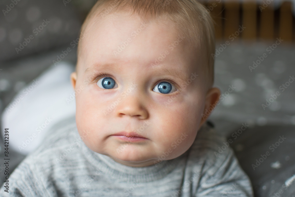 cute blond baby with big blue eyes, baby is laying on bed and looking at camera, closeup portrait of face cute blond baby with big blue eyes, baby is laying on bed and looking at camera, closeup portrait of face