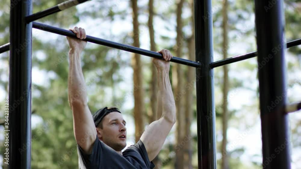 Adult caucasian strong athlete is doing a pull up exercise on a crossbar at the gym at the park during daily workout, side shot Adult caucasian strong athlete is doing a pull up exercise on a crossbar at the gym at the park during daily workout, side shot