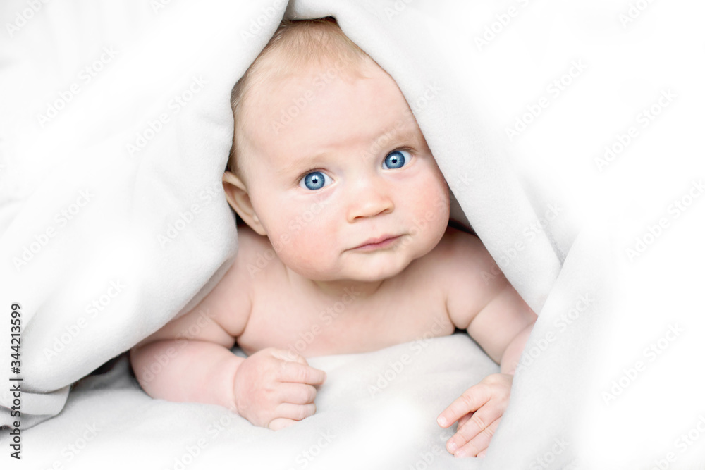 portrait of cute little baby with blue eyes laying under white blanket and smiling, banner copy space, mother's day concept portrait of cute little baby with blue eyes laying under white blanket and smiling, banner copy space, mother's day concept