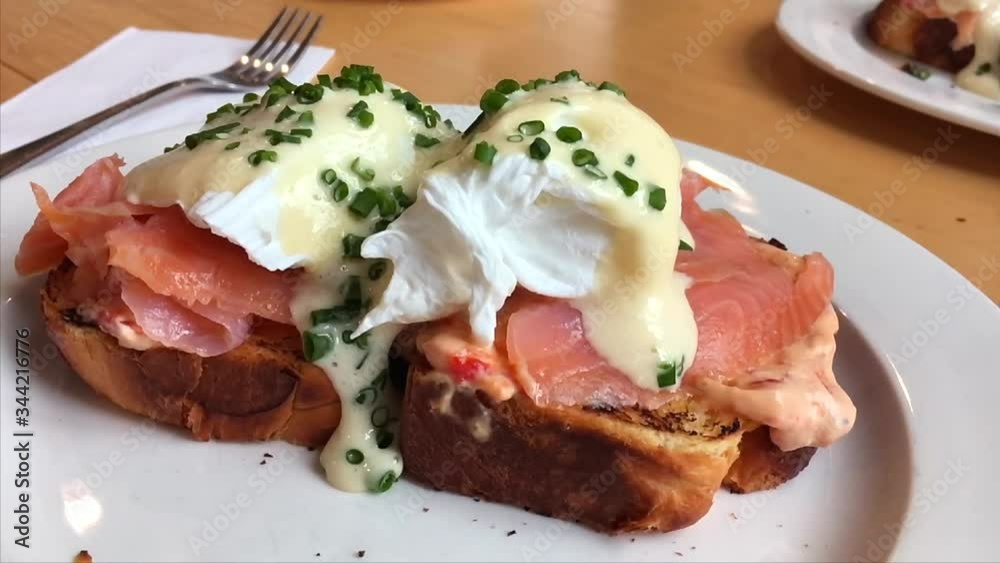 Tasty toast with salmon, poached egg, garlic sauce and chives. Close up. Slow motion.