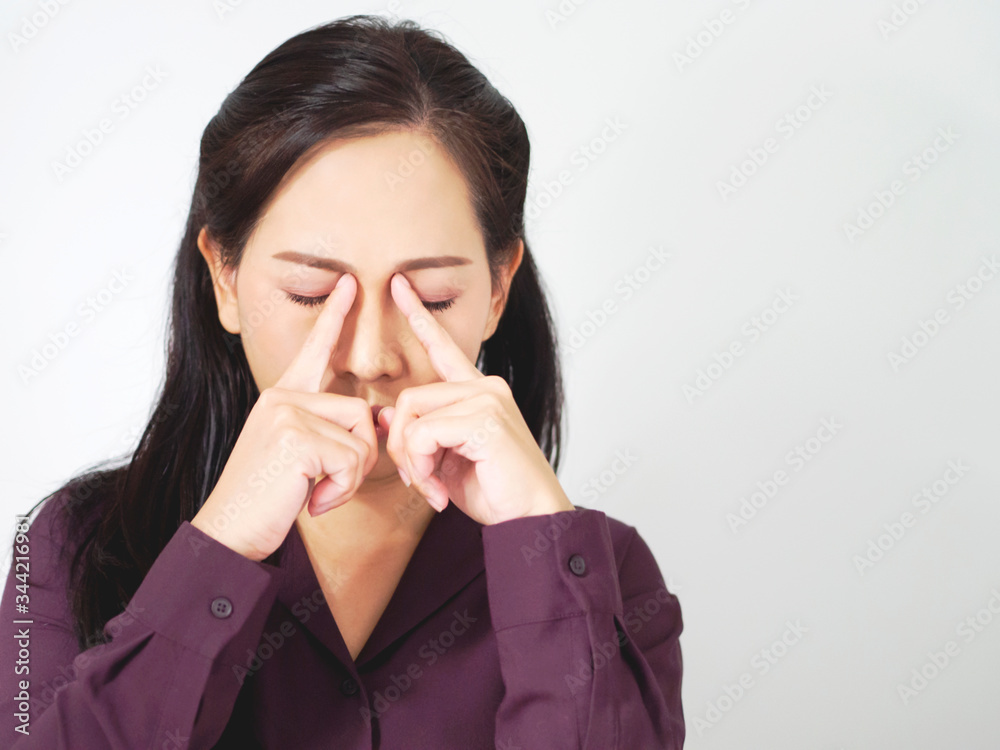 Asian business woman are feeling tired and stressed. Frustrated young worker has dark brown long hair, is massaging nose and closing eyes. Lady wear puple shirt ans standing soft grey background. Asian business woman are feeling tired and stressed. Frustrated young worker has dark brown long hair, is massaging nose and closing eyes. Lady wear puple shirt ans standing soft grey background.