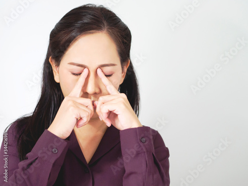 Asian business woman are feeling tired and stressed. Frustrated young worker has dark brown long hair, is massaging nose and closing eyes.  Lady wear puple shirt ans standing soft grey background.