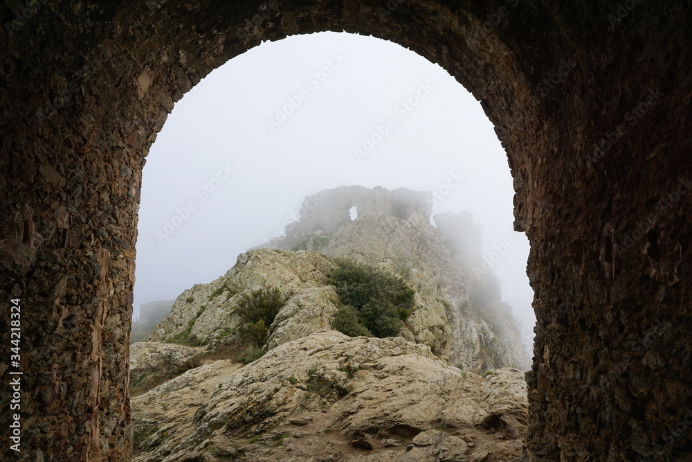 The ruins of the castle de Verdera in the fog seen from under a stone arch, Spain, Catalonia, Alt Emporda, Girona province