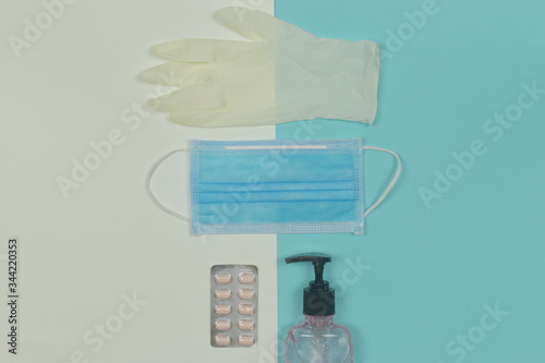 Medical mask with gloves, pills and alcohol gel sanitizer hand gel cleaner on blue background.