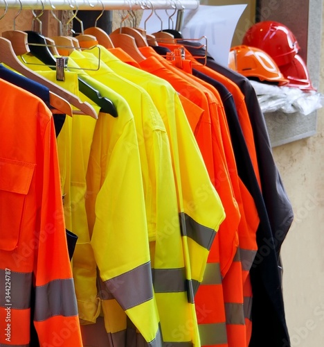 High visibility jackets on a hanger with protective helmets behind, in a work clothes store .