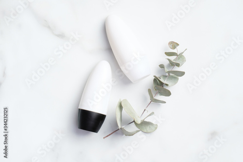 Roll-on deodorant bottles with eucalyptus leaf on marble background. Antiperspirant packaging mockup, sweat protection concept. Flat lay, top view