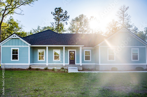 Front view of a brand new construction house with blue siding, a ranch style home with a yard and a sun lens flare