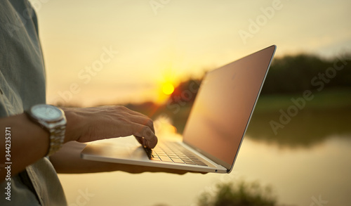 Close-up of a young man using a laptop and the lake and nature at sunset
