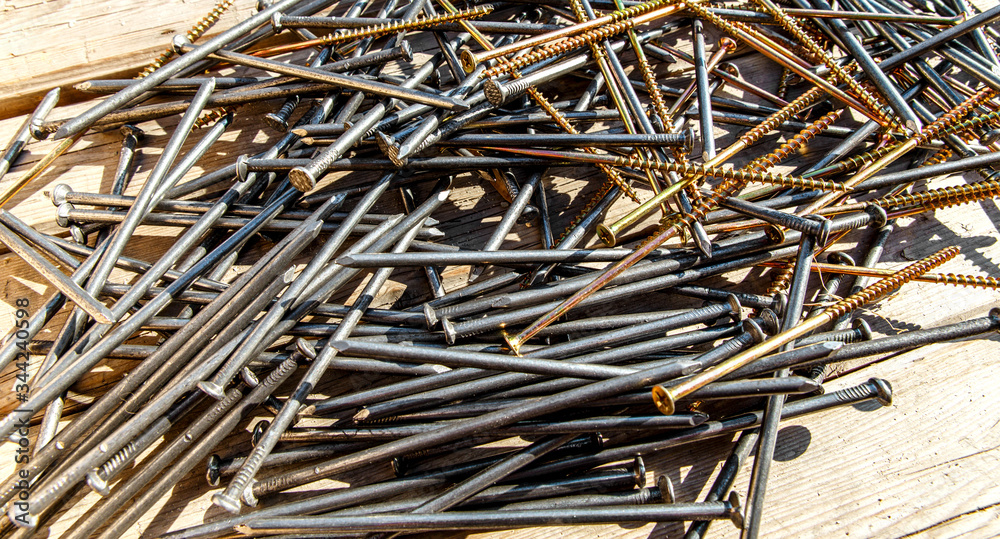 Iron nails and screws on a wooden background. Long, metal, carpenter's nails and self-tapping screws for construction. Fixing tool. The view from the top. Iron nails and screws on a wooden background. Long, metal, carpenter's nails and self-tapping screws for construction. Fixing tool. The view from the top.