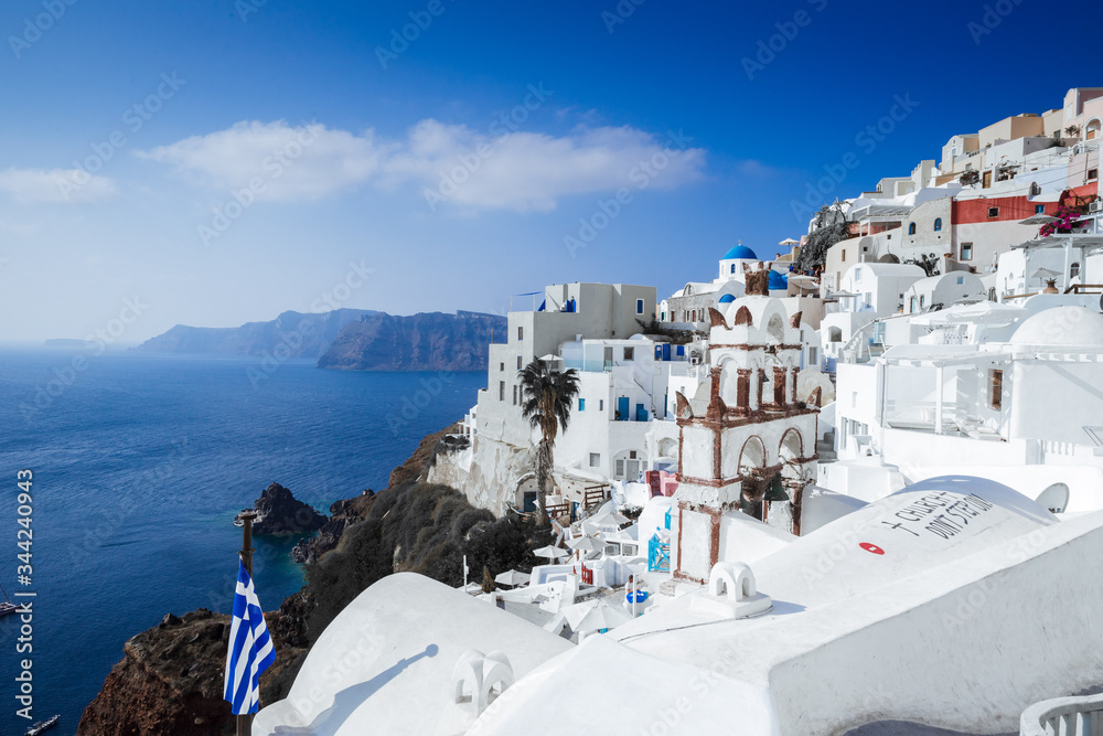 Fototapeta premium Panorama of Oia village, bell tower, Greek flag cliffs with the aegean sea, Santorini island, Cyclades Greece