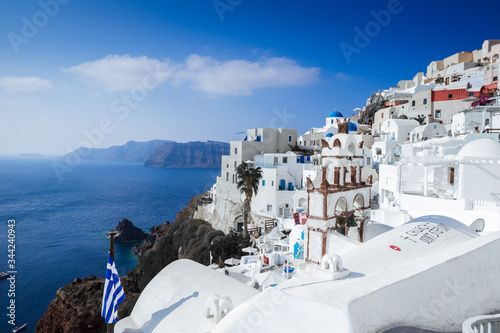 Panorama of Oia village, bell tower, Greek flag cliffs with the aegean sea, Santorini island, Cyclades Greece