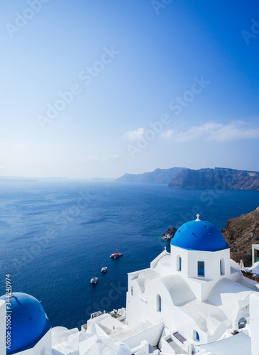 Panorama from Oia, blue domes of orthodox church and the caldera with boats in the back, Santorini island, Cyclades, Greece