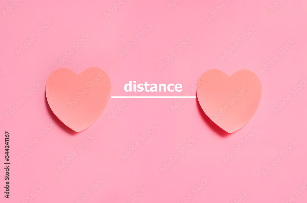Two pink hearts made from paper with distance text on it. Concept of distance between people or lovers or close people
