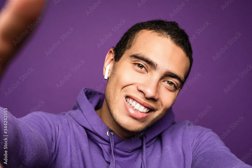 Obraz premium Young funny energetic man doing selfie and smiling. Look from phone. Isolated over purple background. Camera view