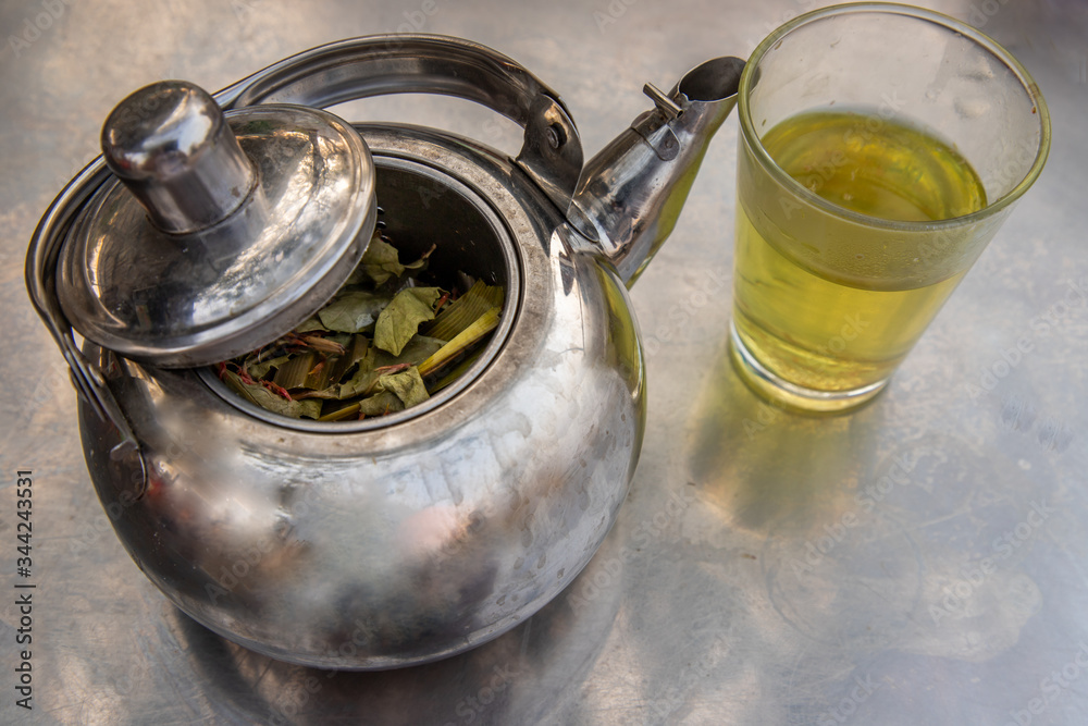 Teapot herbal with glass of hot herbal tea on a stainless steel table. Teapot herbal with glass of hot herbal tea on a stainless steel table.