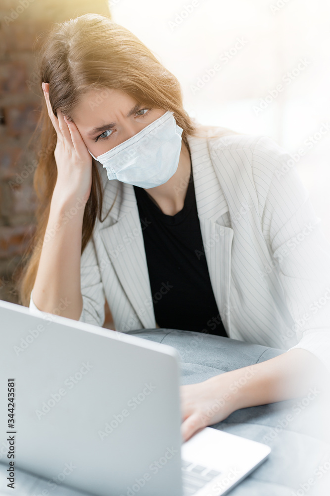 Woman in a jacket and medical mask looks puzzled at the laptops screen trying to solve a work problem. Work at home. Woman in a jacket and medical mask looks puzzled at the laptops screen trying to solve a work problem. Work at home.