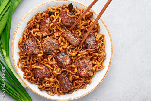 Ram-Don or Chapaguri noodles with beef steak in white bowl on grey concrete backdrop. Jjapaguri is a popular south korean dish with ramen and udon noodles and beef steak. Copy Space