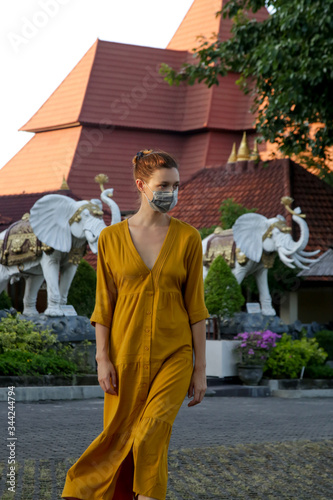 Woman wearing protective medical mask in front of Buddhist temple. Religious hope concept in challenging times. Corona virus outbreak and air pollution concept.