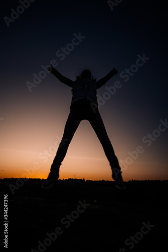 Silhouette of a girl in a jump on a background of sunset and a dark blue sky. The concept of happy people