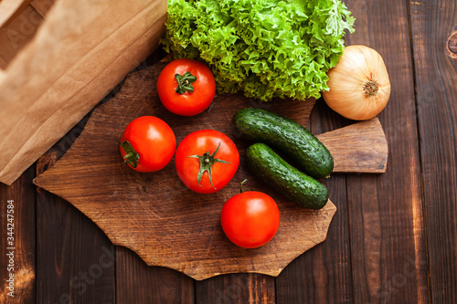 .Tomatoes, cucumbers, lettuce, onions on a cutting board. Paper bag, vegetables, wooden brown background.