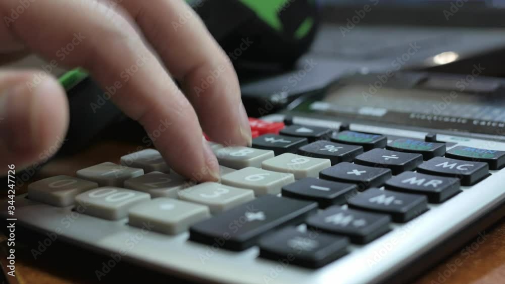 Male fingers print on a calculator in close-up, after which it pays through a manual terminal using a credit card. blur Male fingers print on a calculator in close-up, after which it pays through a manual terminal using a credit card. blur