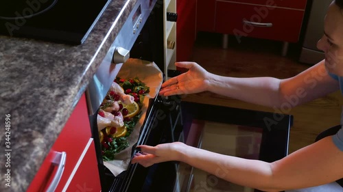 female hands put raw chicken into hot oven