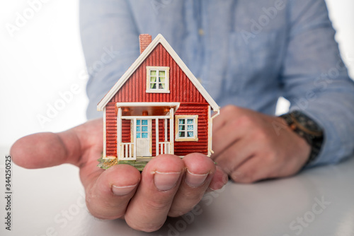 Business man with blue shirt are holding hands over red miniature house to illustrate the importance of insurance and security.