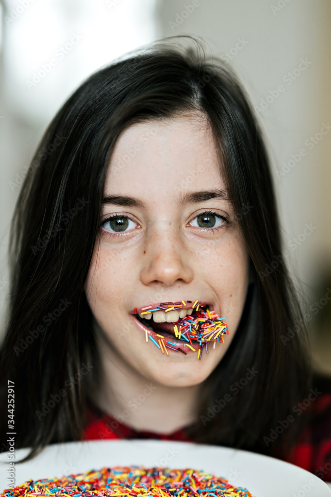 A mischievous and cheerful 8 year old European girl. She shows her tongue. Her lips and tongue are covered in colourful confectionery crumbs.