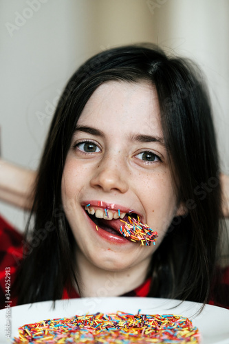 A mischievous and cheerful 8 year old European girl. She shows her tongue. Her lips and tongue are covered in colourful confectionery crumbs.