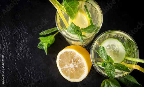 lemonade with yellow lemon, slices of fresh cucumber, green mint and tubes on a black background, copy space, top view