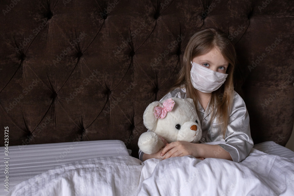 The child is ill. A little girl is sick and hugs a toy in bed. Baby girl lying with teddy bear in mask. Cute little girl in white bed, sad hugging soft bear toy. The child is ill. A little girl is sick and hugs a toy in bed. Baby girl lying with teddy bear in mask. Cute little girl in white bed, sad hugging soft bear toy.