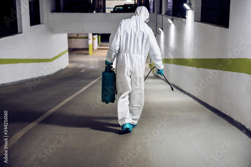 Worker in sterile uniform and mask walking trough underground garage and surface door. Protection from corona virus / covid-19 concept.